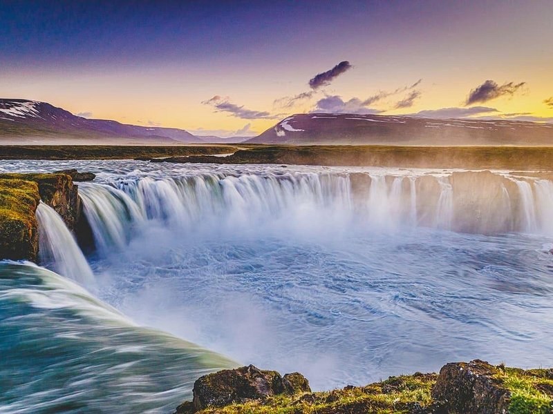 A wide horseshoe waterfall under a pink and gold sunset sky
