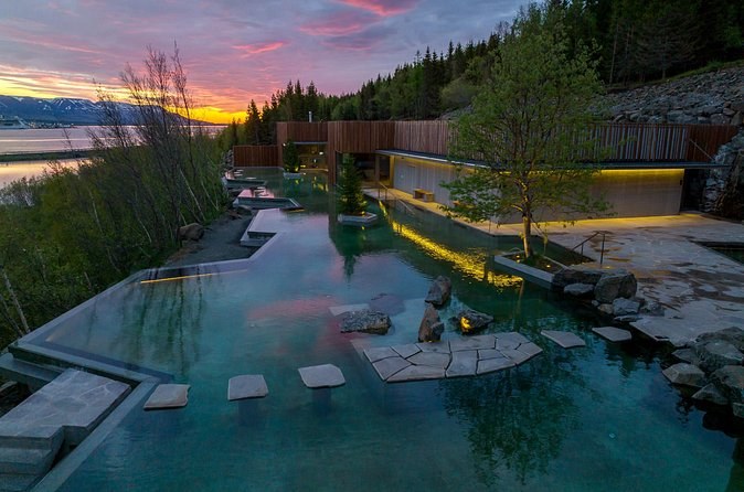 Geothermal pools terraced into a wooded slope above the fjord at dusk