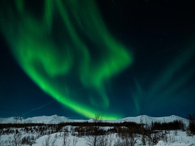 Green northern lights arcing over a snow-covered ridge at night