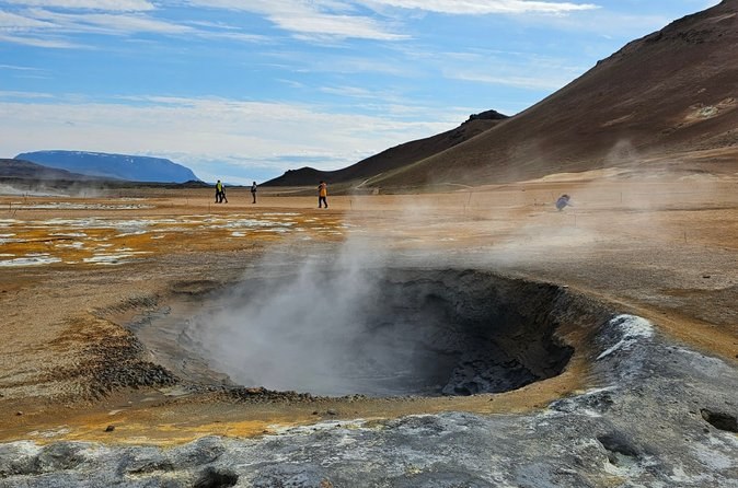 Steam rising from grey mud pools on a bare orange hillside