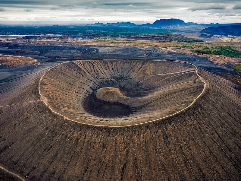 A huge volcanic crater ring seen from the air, a lake and flat moorland beyond